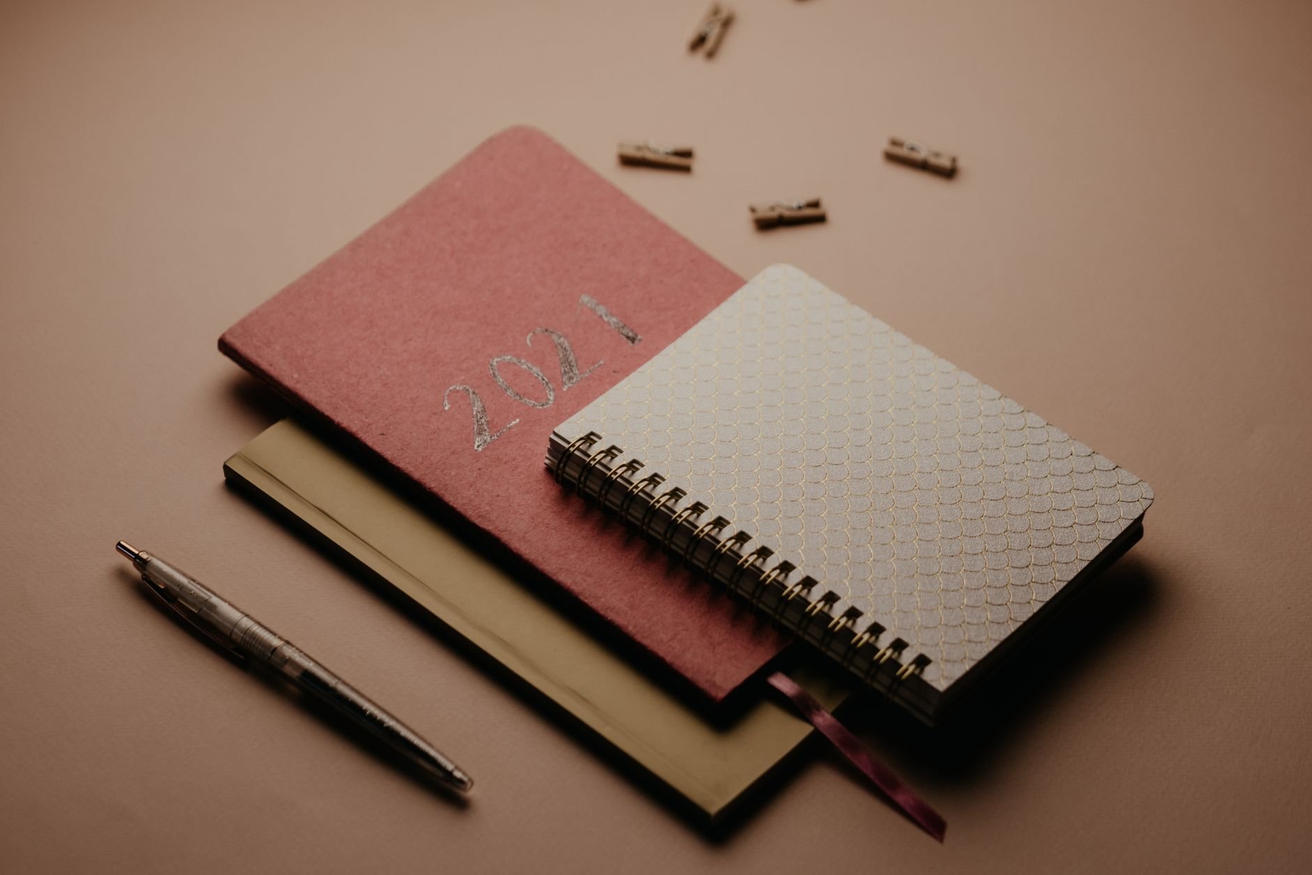 Stylish planner and notebooks arranged with a pen on a warm brown background.